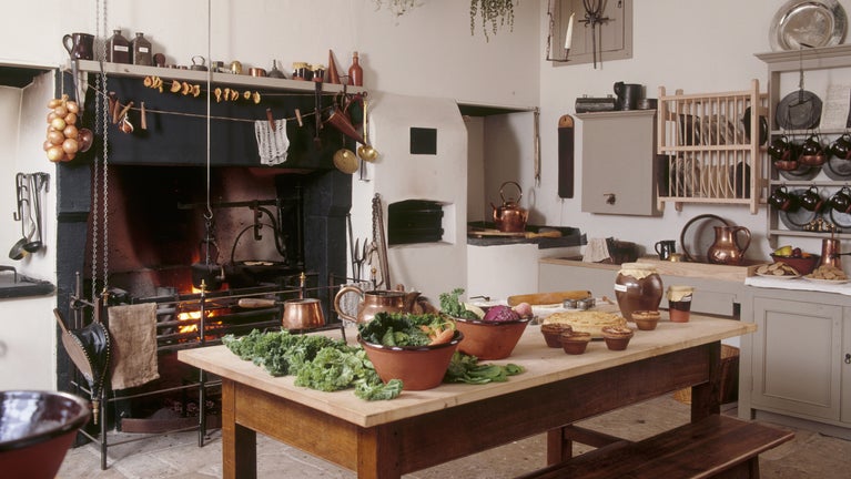 View of the kitchen and fire place where herbs have been brought in to dry and autumn vegetables are being prepared on the table